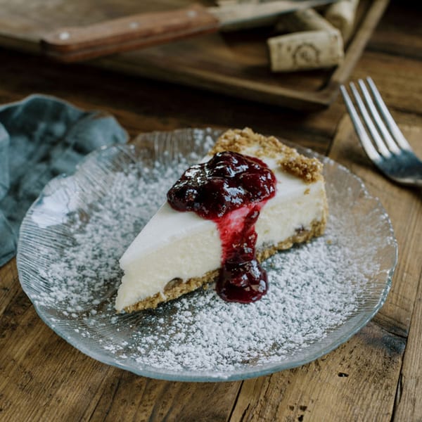 A slice of cheesecake with berry compote and powdered sugar on a glass plate.