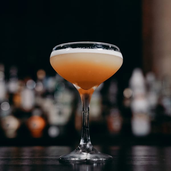 A Frittella Italian Cafe cocktail with foamy top in a coupe glass on a dark bar.