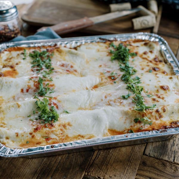 Baked lasagna in a foil pan, topped with melted cheese and fresh parsley, on a wooden table.