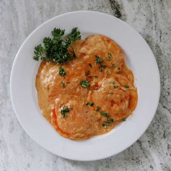 Frittella Italian Cafe's ravioli in a creamy orange sauce, garnished with fresh parsley on a white plate.
