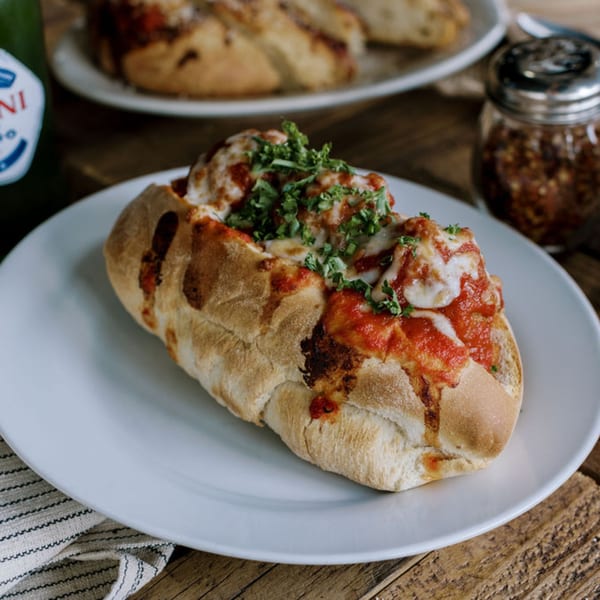 A Frittella Italian Cafe meatball sub with marinara, melted cheese, and parsley on a white plate.