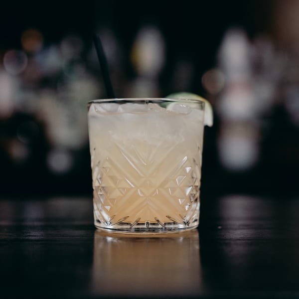 A refreshing cocktail in a cut glass, with ice and a lime wedge, on a dark bar.